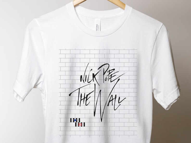 Pode incluir: Camiseta branca com um gr&aacute;fico de parede de tijolo preto e branco e o texto "Nick to the Wall" em preto.