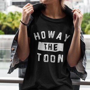 May include: Black t-shirt with white text that reads "Howay the Toon" in a distressed font.