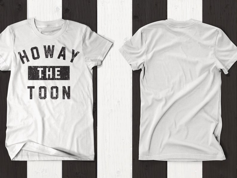 May include: White t-shirt with a black graphic print that says "Howay The Toon". The shirt is shown on a black and white striped background.