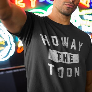 May include: A black t-shirt with white text that reads "HOWAY THE TOON". The text has a distressed, vintage look.