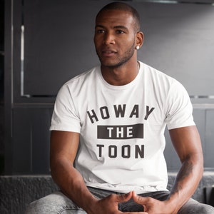Op de afbeelding: Een wit T-shirt met zwarte tekst die "Howay the Toon" zegt.