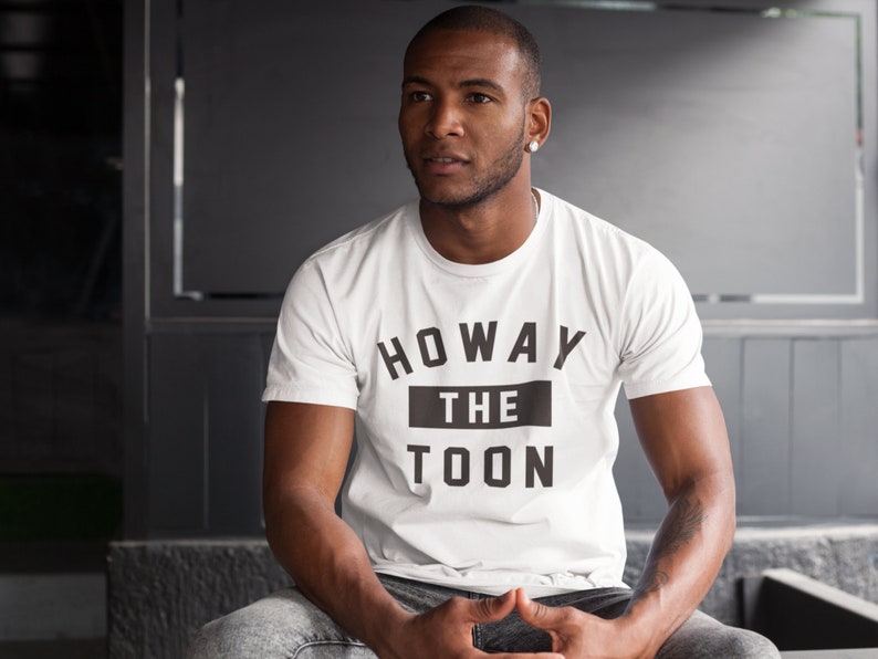 Op de afbeelding: Een wit T-shirt met zwarte tekst die "Howay the Toon" zegt.