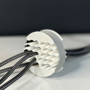 May include: A white plastic cable organizer with a textured surface. Three black cables are threaded through the organizer.