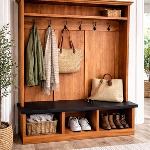 May include: A wooden entryway storage unit with a bench, hooks, and shelves. It features a warm wood finish, a black bench top, and storage cubbies for shoes and baskets. Accessories include bags, a scarf, and a jacket.