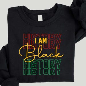 May include: Black sweatshirt with the text "I AM Black HISTORY" in red, yellow, and green. The word "BLACK" is in a bold, stylized font. The sweatshirt is black.