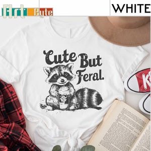 a white shirt with a raccoon holding a cup of coffee