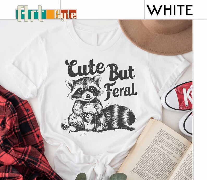a white shirt with a raccoon holding a cup of coffee