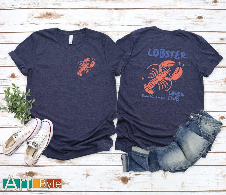 May include: Two navy blue t-shirts with a lobster design. One shirt features a small lobster on the front, the other has a larger lobster graphic with the words "Lobster Lover Club". White trainers and blue jeans are also in the image.