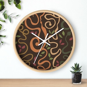 May include: A round wall clock with a light wood frame and a dark brown face. The face features a pattern of winding, abstract lines in shades of orange, tan, and dark green, interspersed with small, scattered red and green leaf-shaped icons.