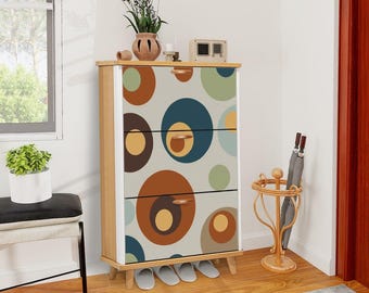 May include: A wooden cabinet with three drawers, featuring a retro design of large, colorful circles in shades of brown, blue, and green against a light background. The cabinet has a light wood frame and is set on short legs.