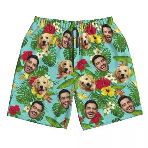 Puede incluir: Ba&ntilde;ador azul con estampado tropical que incluye caras de personas y perros. El estampado incluye hojas verdes, flores rojas y amarillas, y una variedad de otras plantas tropicales.