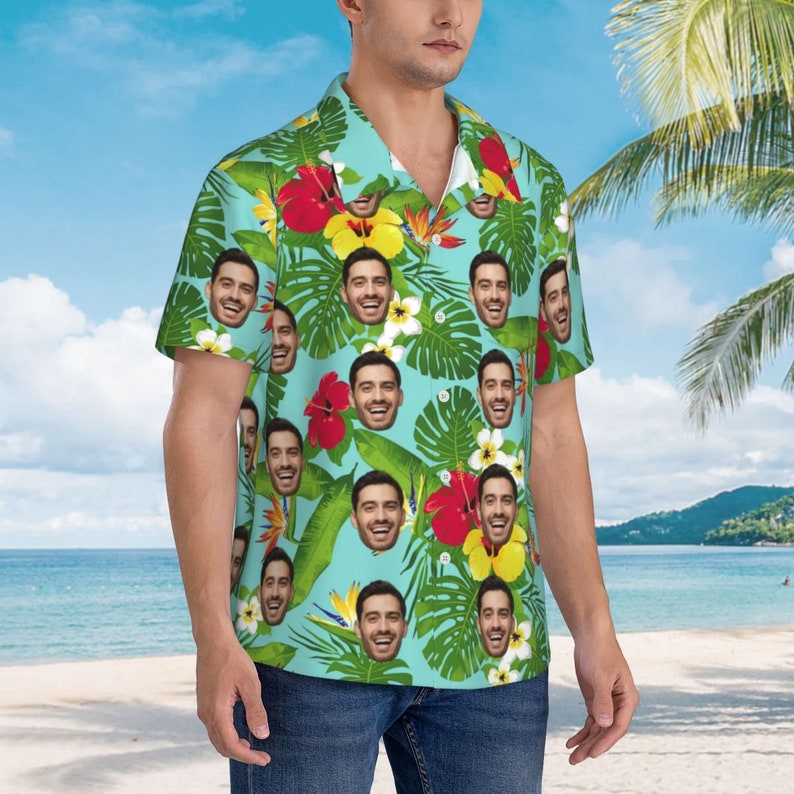Puede incluir: Una camisa azul de manga corta con estampado tropical que presenta m&uacute;ltiples im&aacute;genes de la cara de una persona. La camisa tiene un cuello abotonado y un ajuste holgado.