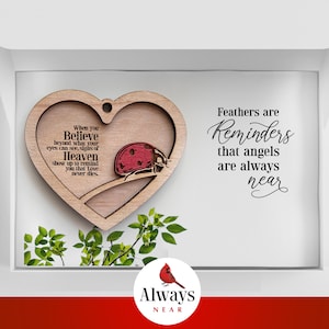 Puede incluir: Adorno de madera en forma de corazón con una mariquita y el texto "When you Believe beyond what your eyes can see, signs of Heaven show up to remind you that Love never dies." El adorno está en una caja blanca con el texto "Feathers are Reminders that angels are always near" y "Always NEAR".