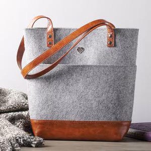 May include: A gray felt tote bag with brown leather handles and trim. The bag has a small diamond-shaped logo on the front.
