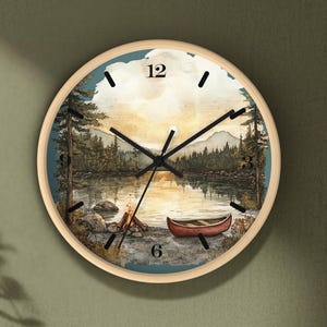 May include: Round wall clock with a nature scene depicting a lake, mountains, and a canoe. The clock face features black hands and numerals against a scenic backdrop. The clock is framed in a light wood finish.