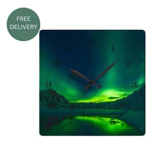 Pode incluir: Um relógio de parede quadrado com uma vibrante aurora boreal verde sobre uma paisagem montanhosa escura e um lago refletor. O mostrador inclui ponteiros pretos e números pretos posicionados ao redor do centro do relógio.