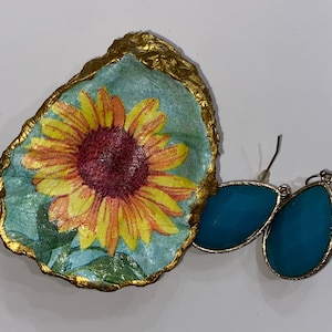 May include: A gold-rimmed dish with a sunflower design and a pair of teal blue earrings.