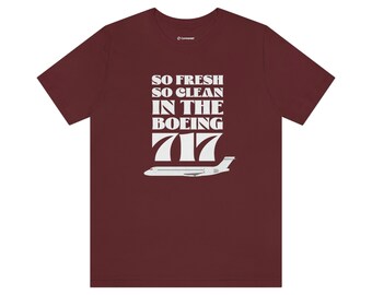 Op de afbeelding: Bordeauxrood T-shirt met witte tekst "SO FRESH SO CLEAN IN THE BOEING 717" en een witte vliegtuigafbeelding. Het T-shirt heeft een ronde hals.