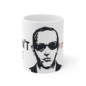 May include: White ceramic mug featuring a black and white graphic of a man wearing sunglasses. The mug has the text "I DON'T SEE IT" in black, with "(IT)" in red.
