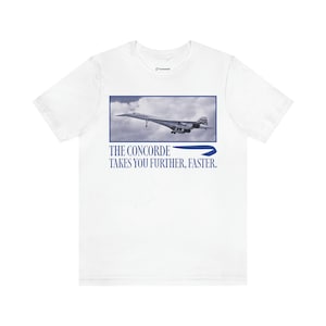 May include: White t-shirt featuring a graphic of the Concorde supersonic jet in flight, set against a cloudy sky within a blue rectangle. Below the image, the text reads "THE CONCORDE TAKES YOU FURTHER, FASTER."