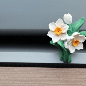 May include: A ceramic flower bouquet with white and yellow petals and green leaves. The flowers are arranged in a cluster and have a realistic appearance.