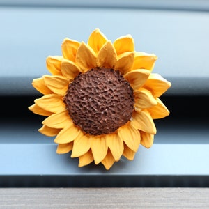 May include: A yellow and brown artificial sunflower with a textured centre. The sunflower is attached to a blue surface.
