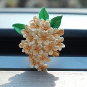 May include: A white and cream-coloured flower bouquet with green leaves. The bouquet is made of artificial flowers and is designed to look like a bunch of lilacs.