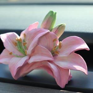 May include: A pink lily flower with green stems and yellow pollen. The flower is sitting on a dark grey surface.