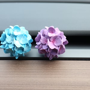 May include: Two small, round, artificial flower arrangements. One is light blue and the other is purple.