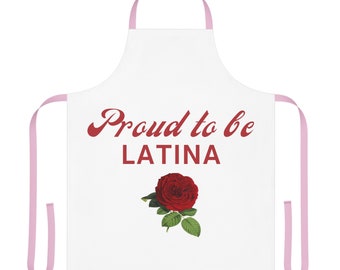 May include: A white apron with light pink neck and waist ties. The front features the red text "Proud to be LATINA" positioned above a detailed illustration of a single red rose with green leaves centred on the lower portion of the fabric.