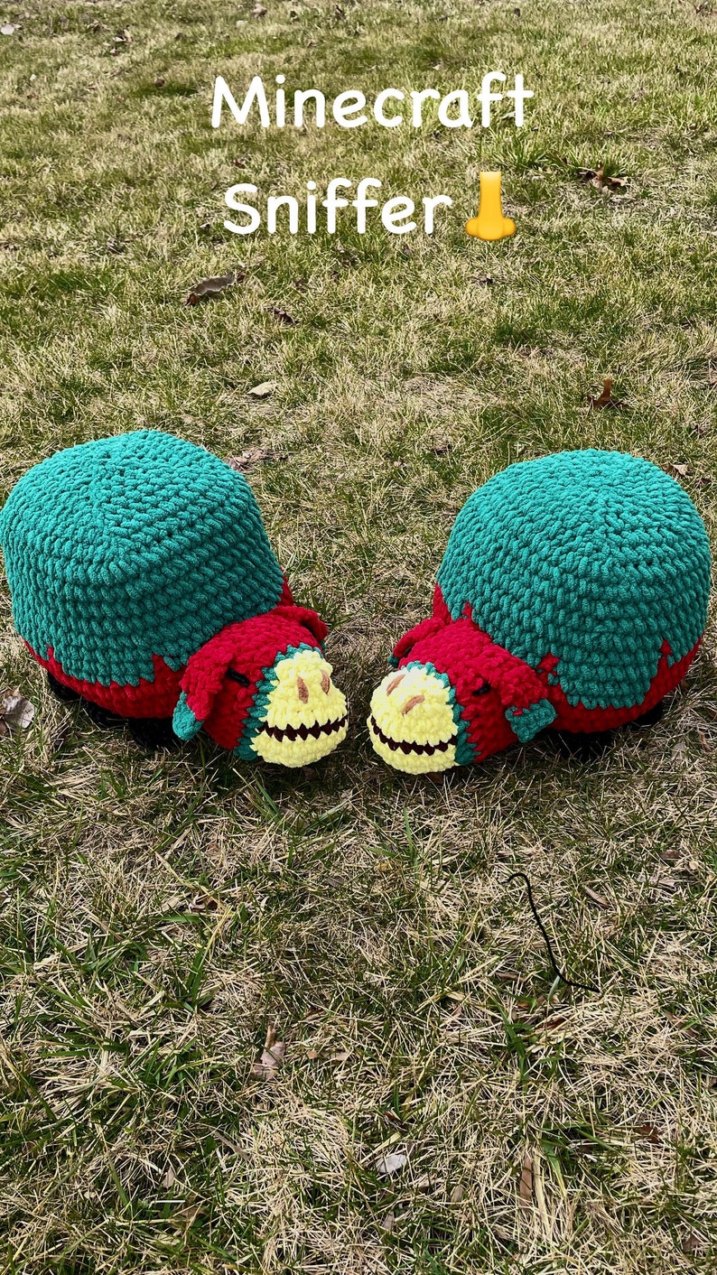 May include: Two crocheted Minecraft Sniffer plushies. The plushies are green, red, and yellow. They are sitting on a bed of green grass.