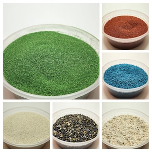 May include: Six bowls of different colored sand. The bowls are white plastic and contain green, red, blue, white, black, and beige sand.