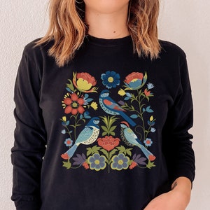 May include: A black long-sleeved sweatshirt with a colorful floral and bird design. The design features blue, red, yellow, green, and white colors.