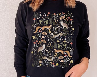 May include: Black long-sleeved sweatshirt with a colorful woodland creature print featuring owls, squirrels, and rabbits. The print includes mushrooms, leaves, and stars.