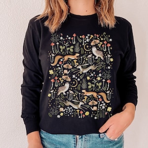 May include: Black long-sleeved sweatshirt with a colorful woodland creature print featuring owls, squirrels, and rabbits. The print includes mushrooms, leaves, and stars.