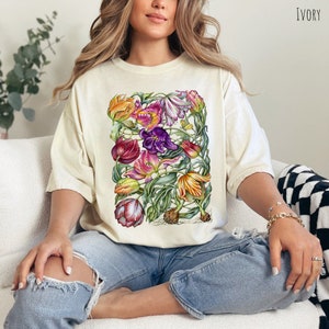 Op de afbeelding: Een wit T-shirt met een bloemenprint van tulpen in tinten roze, paars, geel en groen. Het shirt heeft een relaxte pasvorm en een ronde hals.