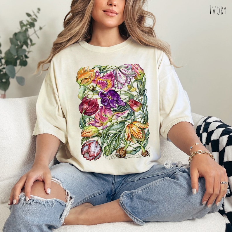 Op de afbeelding: Een wit T-shirt met een bloemenprint van tulpen in tinten roze, paars, geel en groen. Het shirt heeft een relaxte pasvorm en een ronde hals.