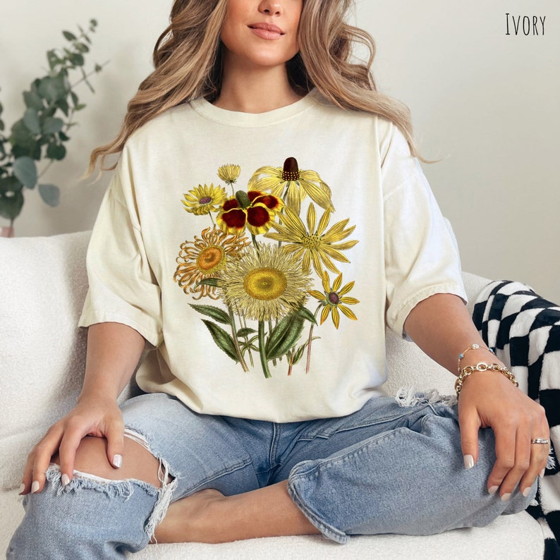 Op de afbeelding: Een wit T-shirt met een bloemenprint van gele, rode en bruine bloemen. De bloemen zijn in een boeket gerangschikt en hebben een vintage stijl.