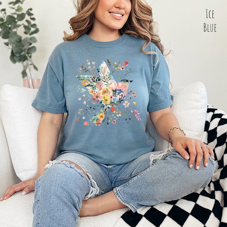 Op de afbeelding: Een blauw T-shirt met een bloemenprint met een vogel. De vogel is gemaakt van bloemen en bladeren in roze, gele en groene tinten. Het shirt heeft een ontspannen pasvorm en een ronde hals.