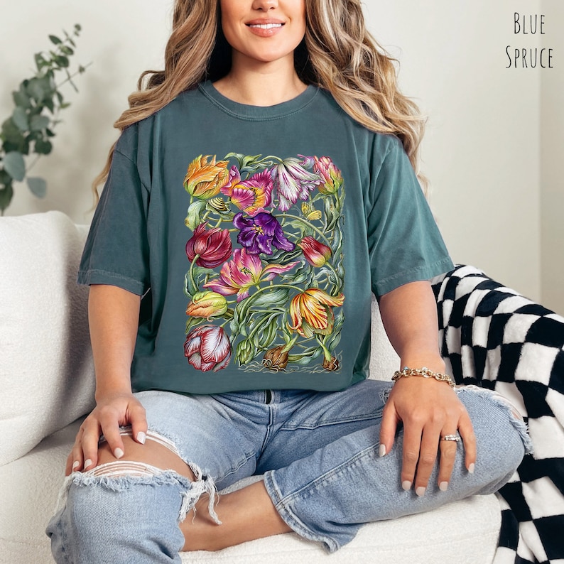 Op de afbeelding: Een tealblauw t-shirt met een kleurrijke bloemenprint van tulpen. De print bevat een verscheidenheid aan kleuren, waaronder roze, paars, geel, oranje en rood. Het shirt is gemaakt van een zachte, comfortabele stof en heeft een ontspannen pasvorm.