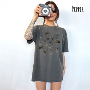 May include: An oversized t-shirt in a dark grey colour with a graphic print of a spider web with spiders in the centre. The text "PEPPER" is in the top right corner of the image.