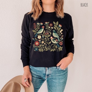 May include: Black long-sleeved shirt with a colorful floral and bird design. The design features a tree with flowers, leaves, and birds in shades of blue, green, red, and yellow.
