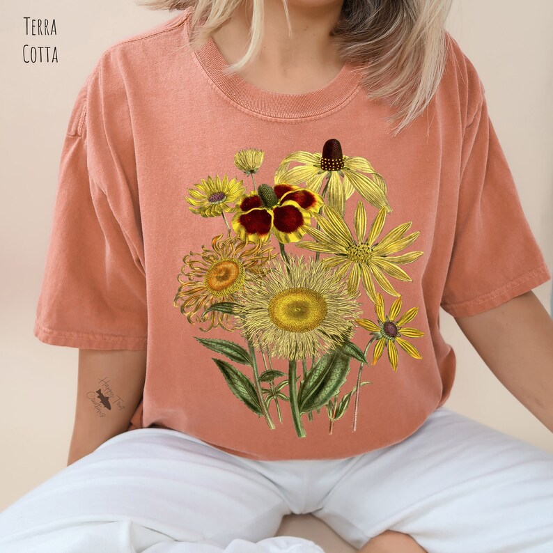 Op de afbeelding: Een terracotta oranje T-shirt met een vintage bloemenprint met gele, rode en groene bloemen. De bloemen zijn in een boeket op de voorkant van het shirt gerangschikt.