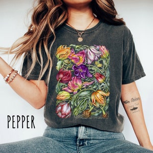 Op de afbeelding: Een donkergrijs T-shirt met een kleurrijke bloemenprint van tulpen. De print bevat een verscheidenheid aan kleuren, waaronder rood, roze, paars, geel en groen. Het shirt heeft een ronde hals en korte mouwen. De tekst "More Dreams Happy That Creations" is gedrukt op de rechtermouw van het shirt.
