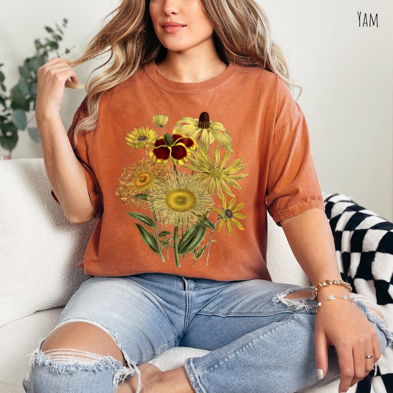 Op de afbeelding: Een oranje T-shirt met een vintage bloemenprint met gele, bruine en rode bloemen.
