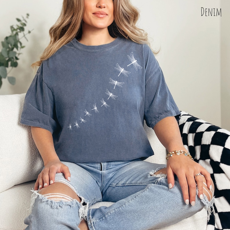 May include: A blue oversized t-shirt with a white dragonfly design. The shirt is made of a soft, comfortable fabric and has a relaxed fit.