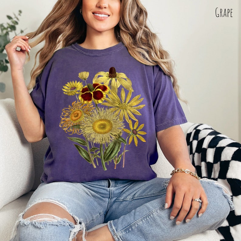 Op de afbeelding: Een paars T-shirt met een vintage bloemenprint met gele, bruine en rode bloemen. De bloemen zijn in een boeket gerangschikt en hebben een gedetailleerde, realistische stijl.