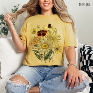 Op de afbeelding: Een mosterdgeel T-shirt met een vintage bloemenprint met zonnebloemen, madeliefjes en andere wilde bloemen in tinten geel, bruin en rood.