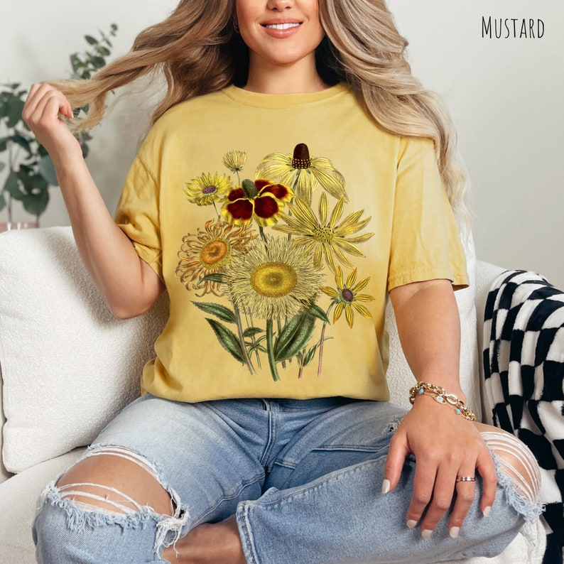 Op de afbeelding: Een mosterdgeel T-shirt met een vintage bloemenprint met zonnebloemen, madeliefjes en andere wilde bloemen in tinten geel, bruin en rood.