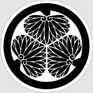 Puede incluir: Una pegatina circular en blanco y negro con un escudo floral estilizado. El diseño consta de tres grupos de flores estilizadas dispuestas en un patrón triangular dentro de un círculo negro.